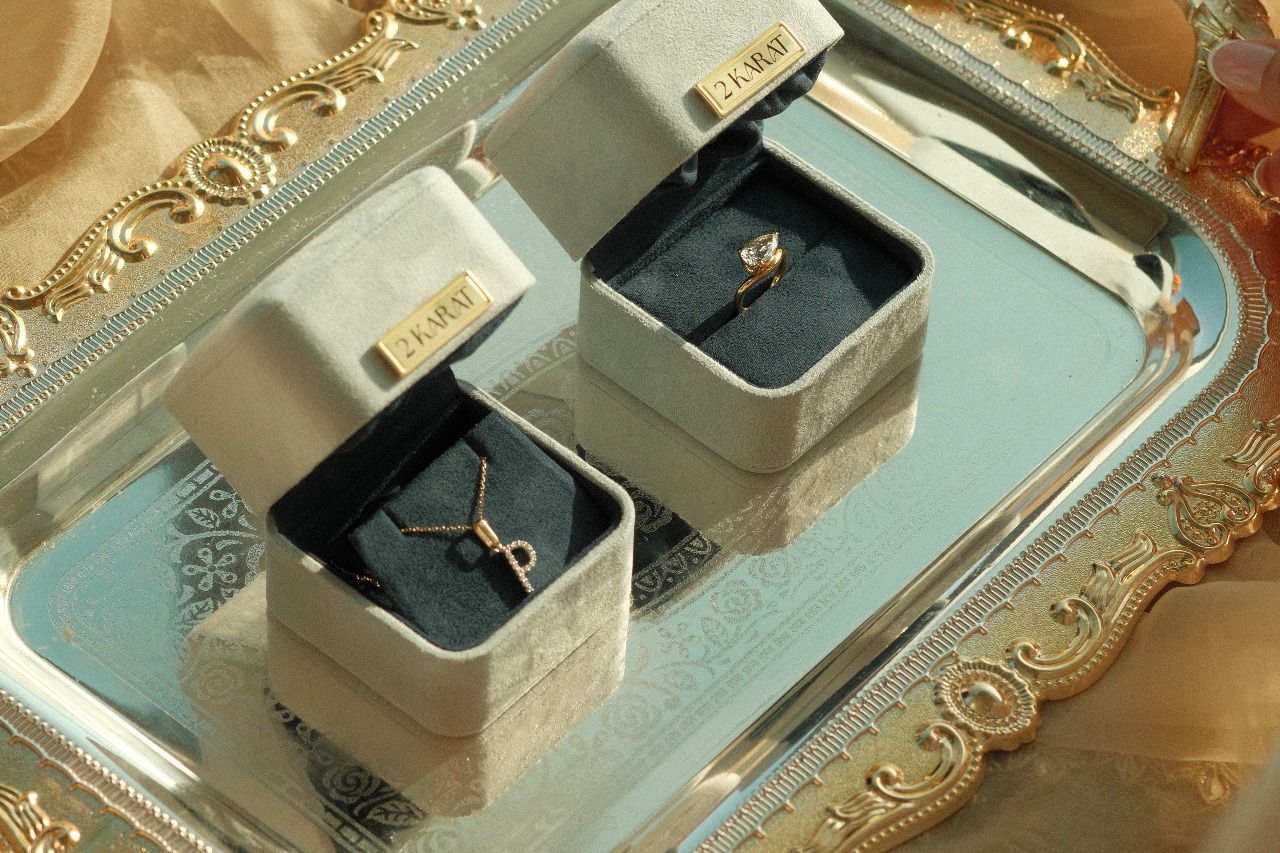 2 Karat velvet ring boxes with an engagement ring and fine jewellery pendant on an ornate gold tray